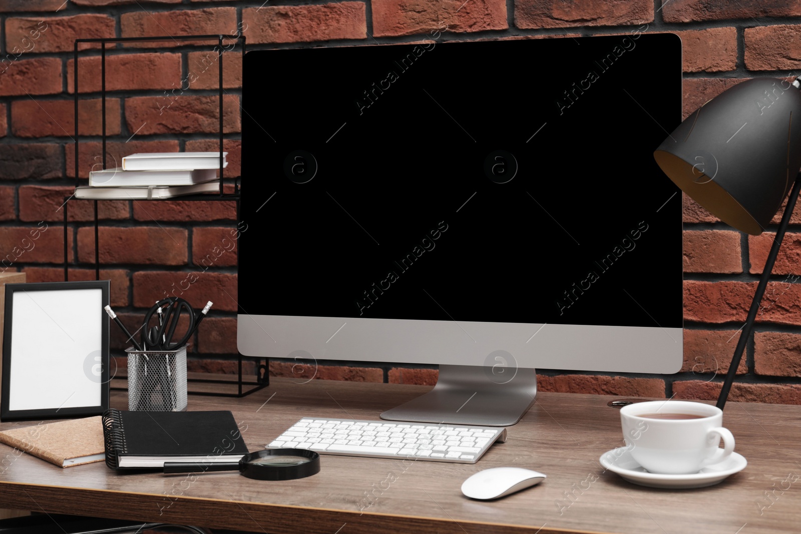 Photo of Cosy workspace with computer, lamp and stationery on desk near brick wall at home