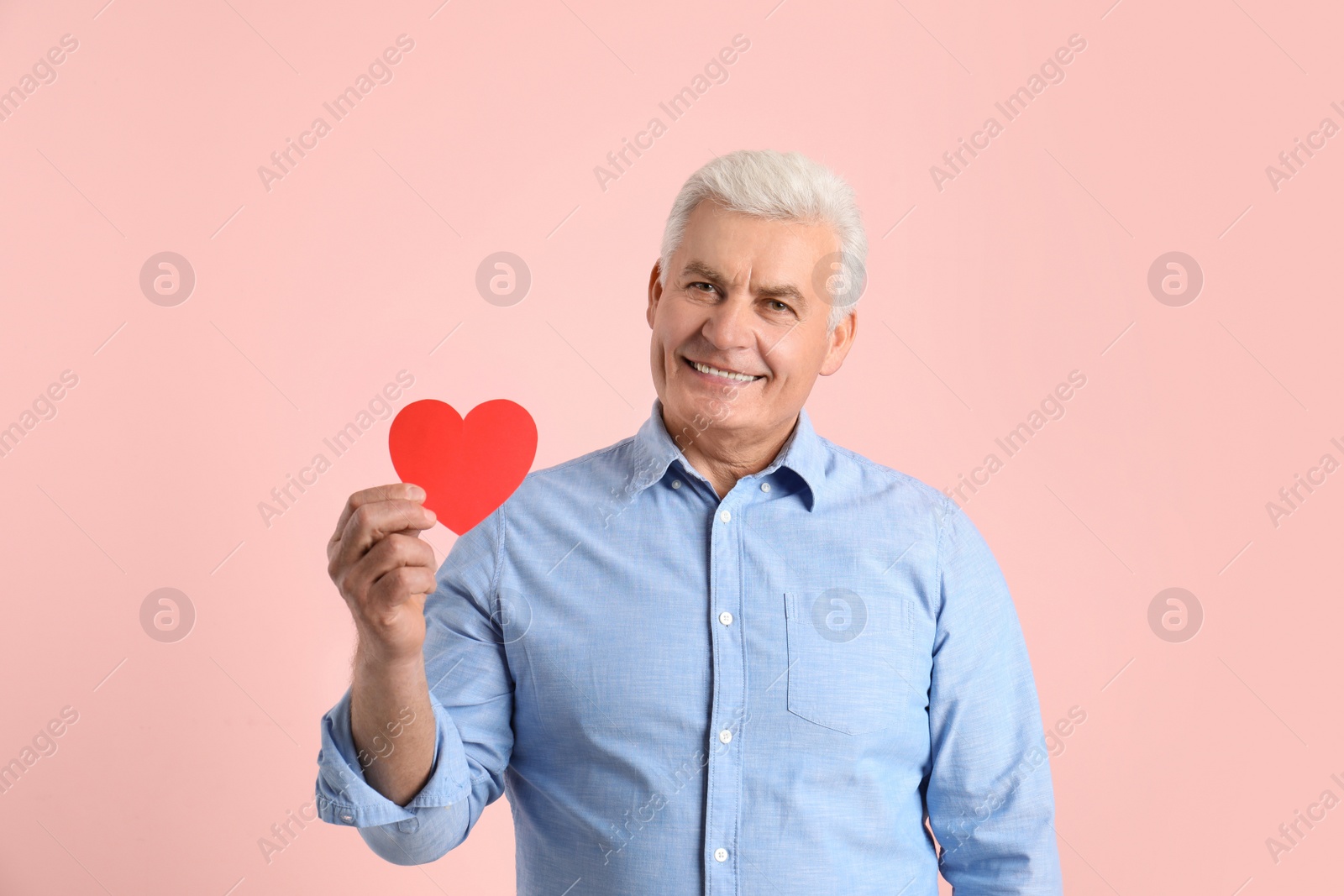 Photo of Happy mature man holding red paper heart on color background