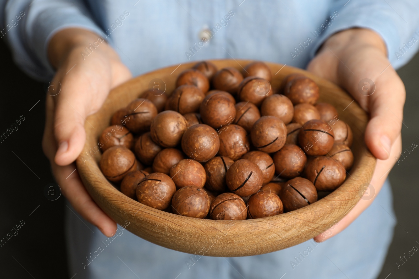 Photo of Woman holding plate with organic Macadamia nuts, closeup
