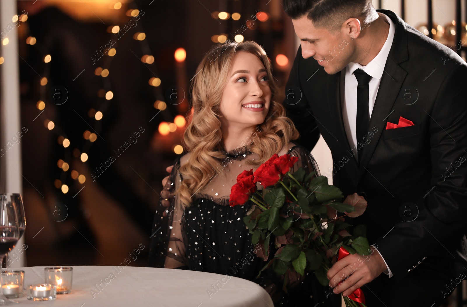 Photo of Man presenting roses to his beloved woman in restaurant at Valentine's day dinner