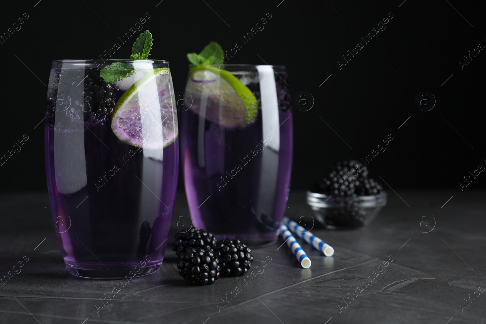 Photo of Delicious blackberry lemonade made with soda water and ingredients on grey table, closeup