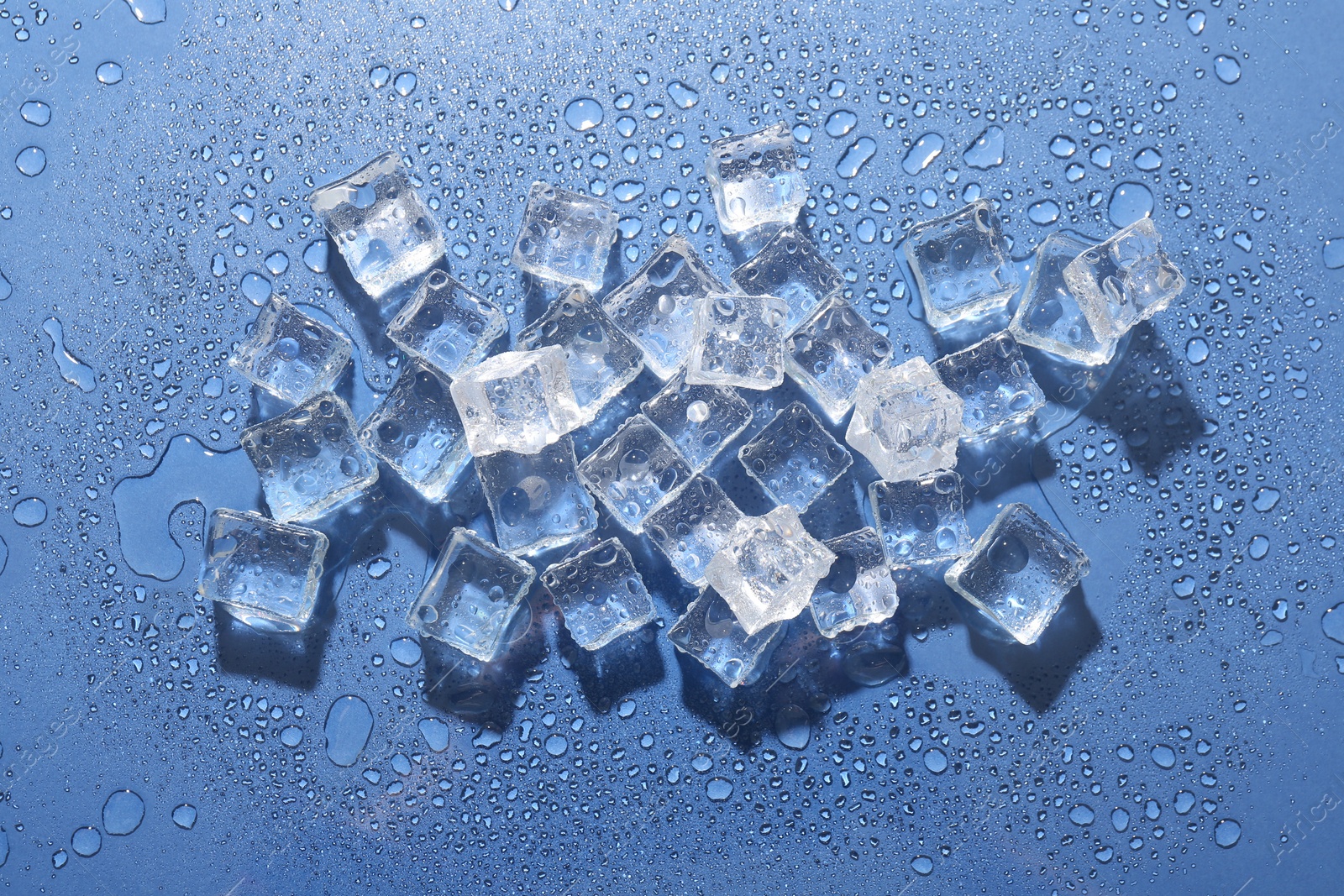 Photo of Melting ice cubes and water drops on blue background, flat lay