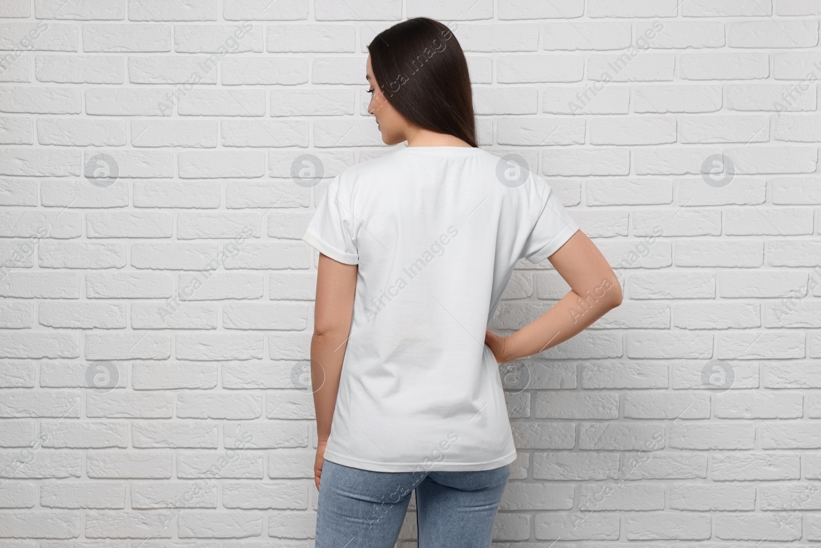 Photo of Woman wearing stylish T-shirt near white brick wall, back view