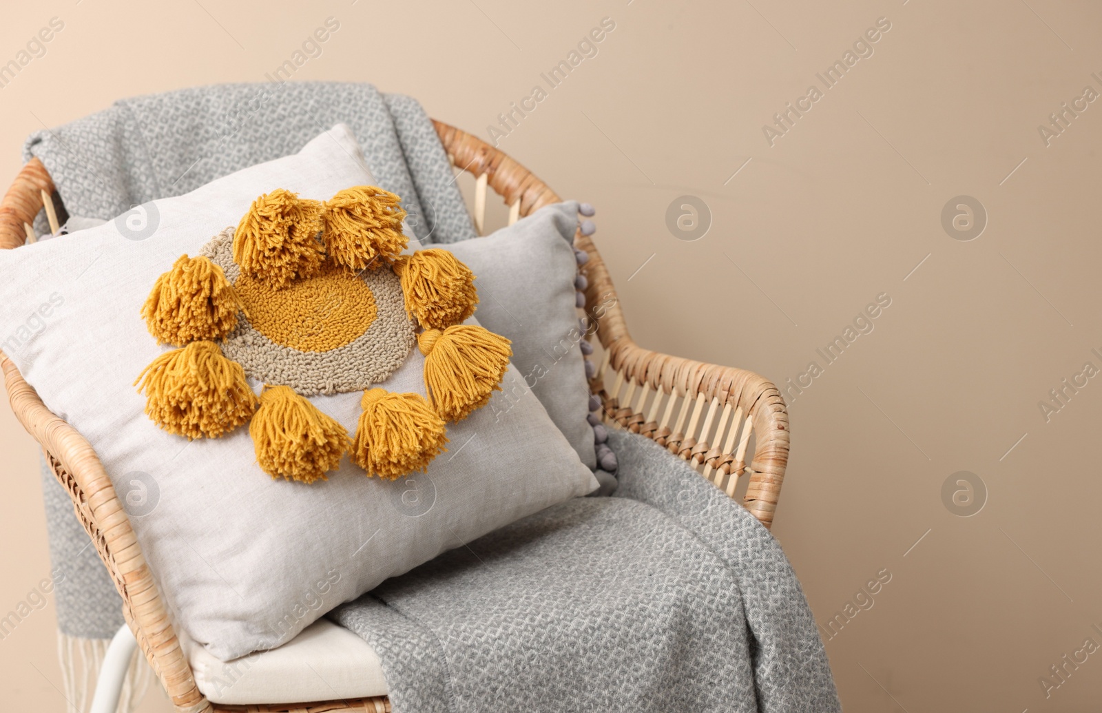 Photo of Stylish soft pillow and blanket on armchair near beige wall. Space for text