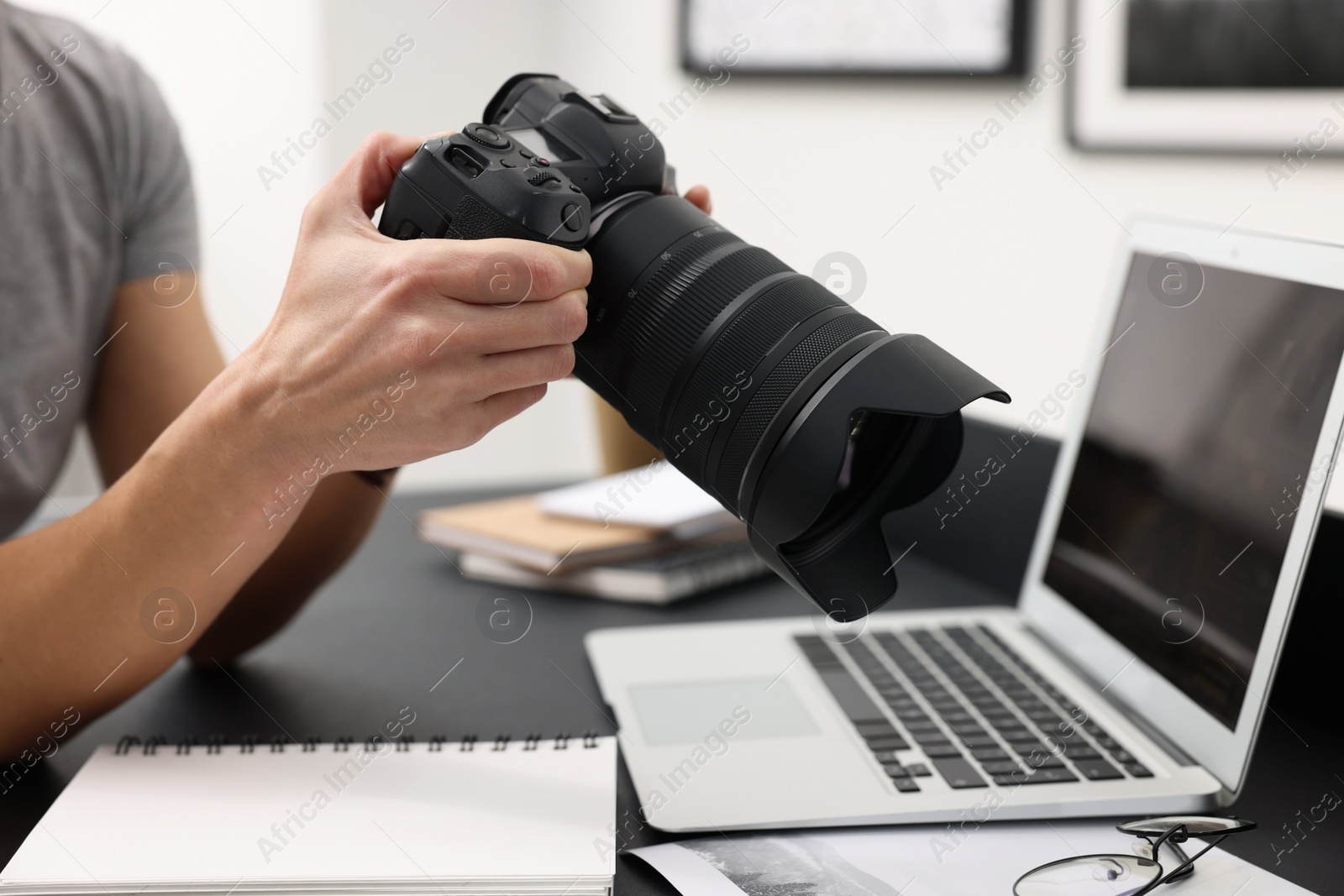 Photo of Professional photographer with digital camera at table indoors, closeup