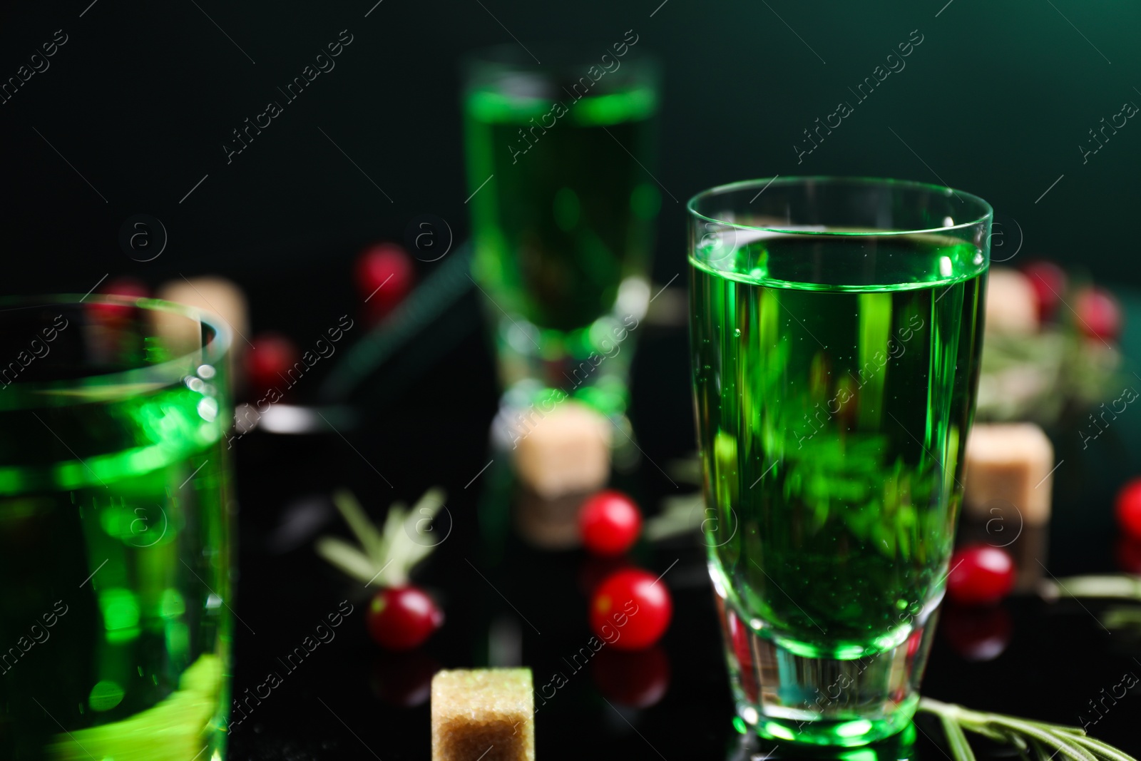 Photo of Absinthe in shot glass, cranberries and brown sugar on mirror table, closeup. Alcoholic drink