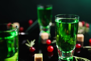 Absinthe in shot glass, cranberries and brown sugar on mirror table, closeup. Alcoholic drink