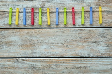 Colorful plastic clothespins and rope on wooden background, top view. Space for text