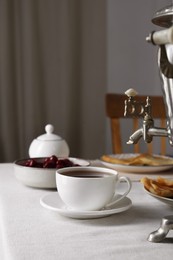 Photo of Vintage samovar, cup of hot drink and snacks served on table indoors. Traditional Russian tea ceremony