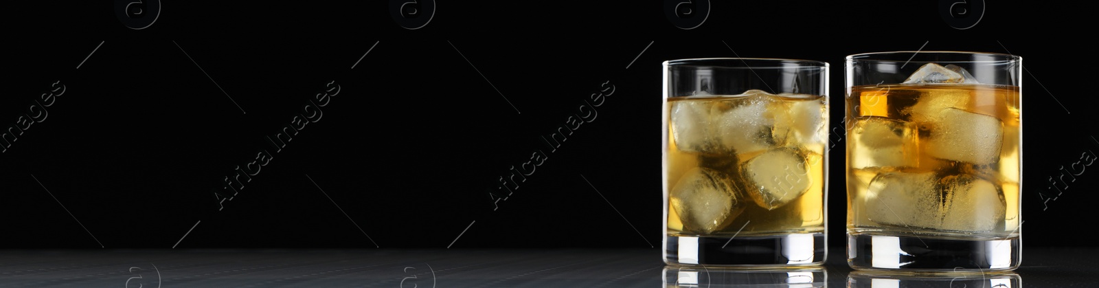 Image of Whiskey and ice cubes in glasses on grey table against black background, space for text. Banner design