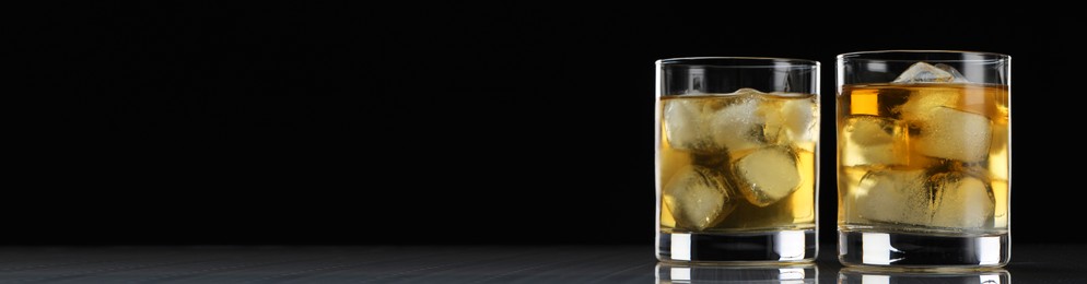 Image of Whiskey and ice cubes in glasses on grey table against black background, space for text. Banner design