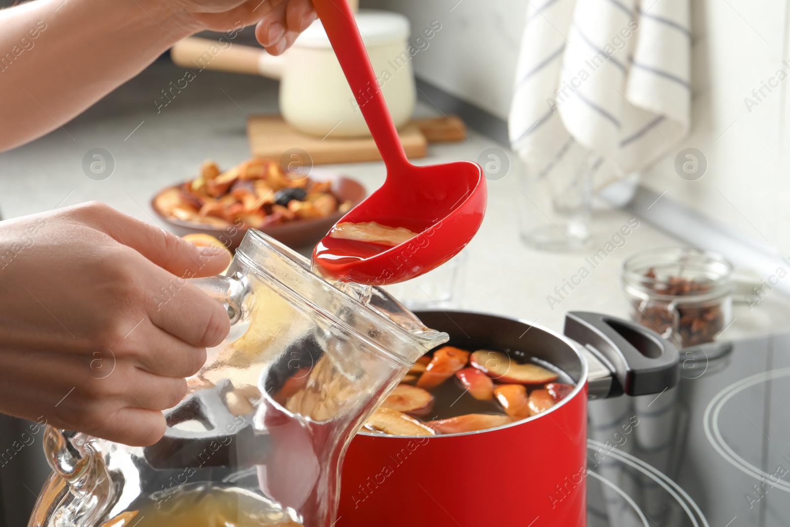 Photo of Woman pouring compot into glass pitcher near stove, closeup