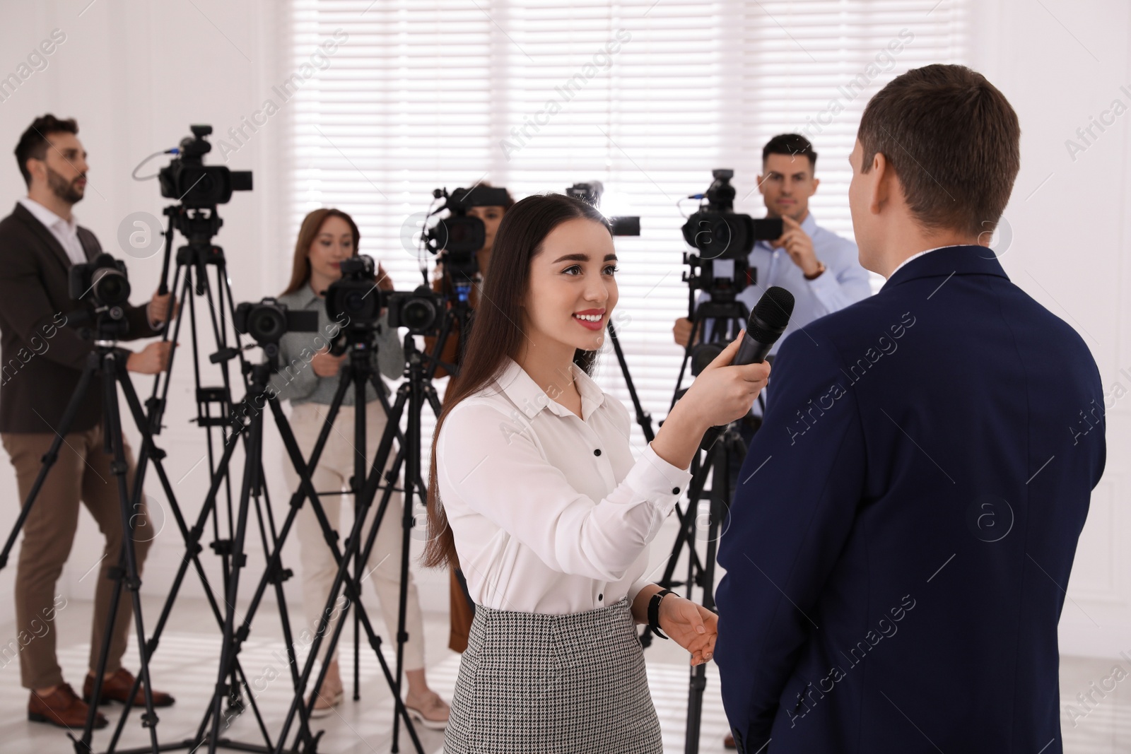 Photo of Professional young journalist interviewing businessman and group of video camera operators on background