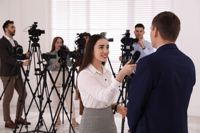 Photo of Professional young journalist interviewing businessman and groupvideo camera operators on background