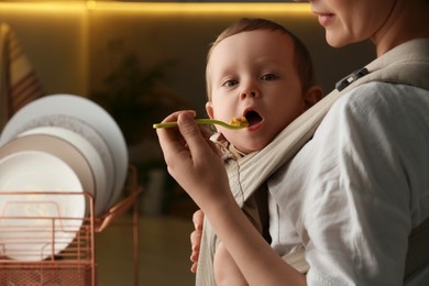 Photo of Mother feeding her cute child in sling (baby carrier at home