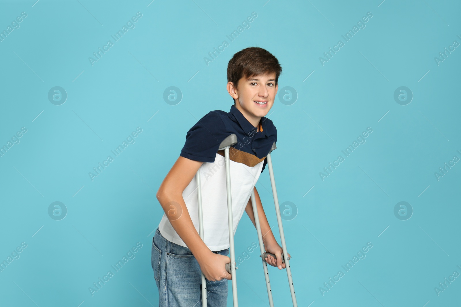 Photo of Teenage boy with injured leg using crutches on turquoise background