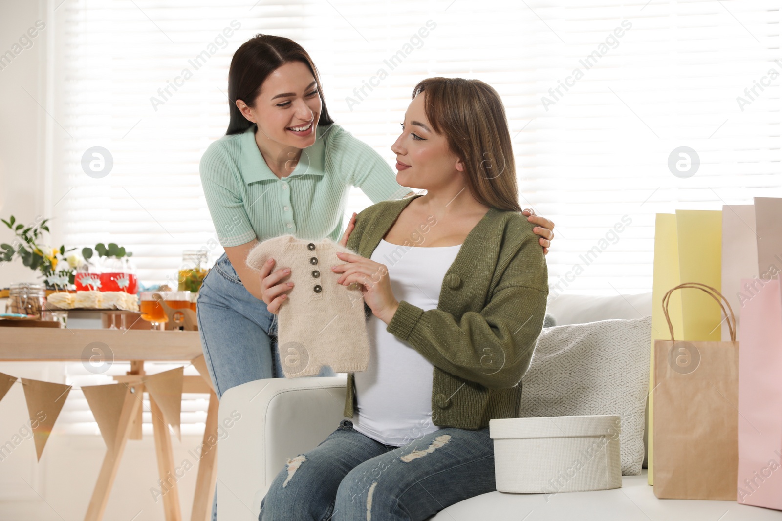 Photo of Happy pregnant woman and her friend with gift at baby shower party