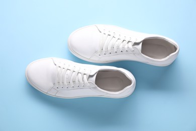 Pair of stylish white sneakers on light blue background, top view