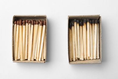 Cardboard boxes with whole and burnt matches on white background, top view