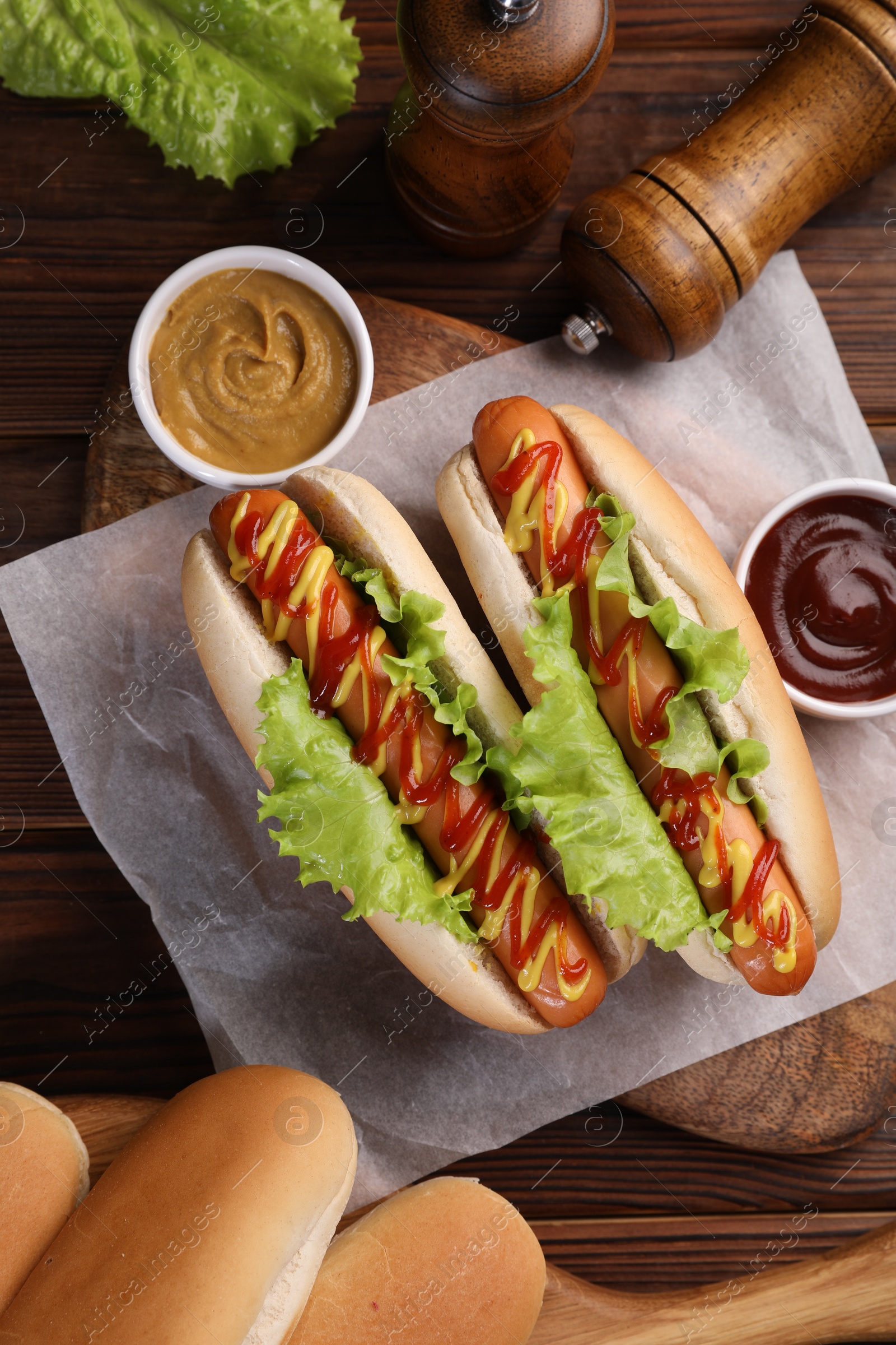 Photo of Tasty hot dogs with lettuce, ketchup and mustard on wooden table, flat lay