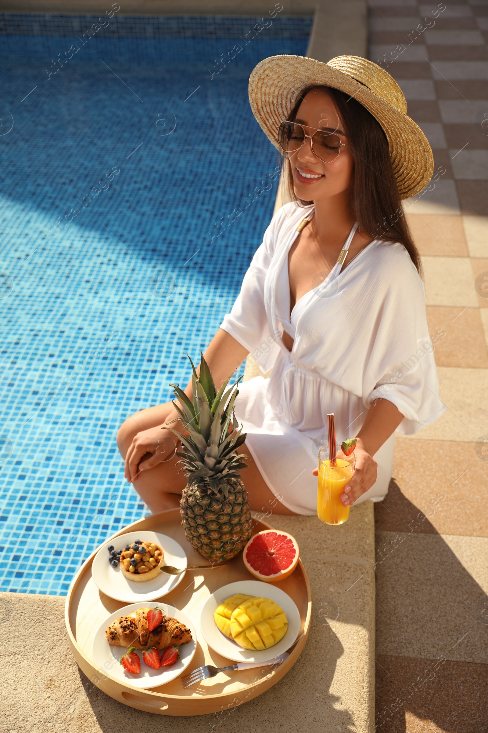 Photo of Young woman with delicious breakfast on tray near swimming pool