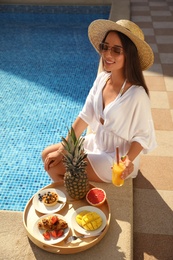 Young woman with delicious breakfast on tray near swimming pool