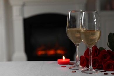 Photo of Glasses of white wine, burning candle and rose flowers on grey table indoors, space for text. Romantic atmosphere