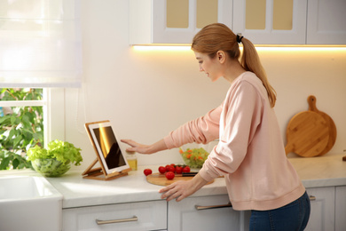 Photo of Young woman with tablet cooking at counter in kitchen