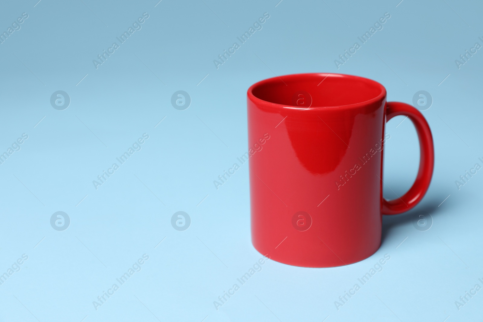 Red ceramic mug on light blue background, space for text Photo of Red ceramic mug on light blue background, space for text