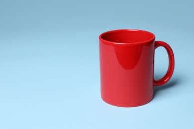 Photo of Red ceramic mug on light blue background, space for text