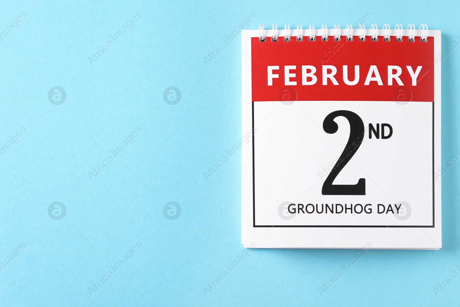 Photo of Top view of calendar with date February 2nd on light blue background, space for text. Groundhog day