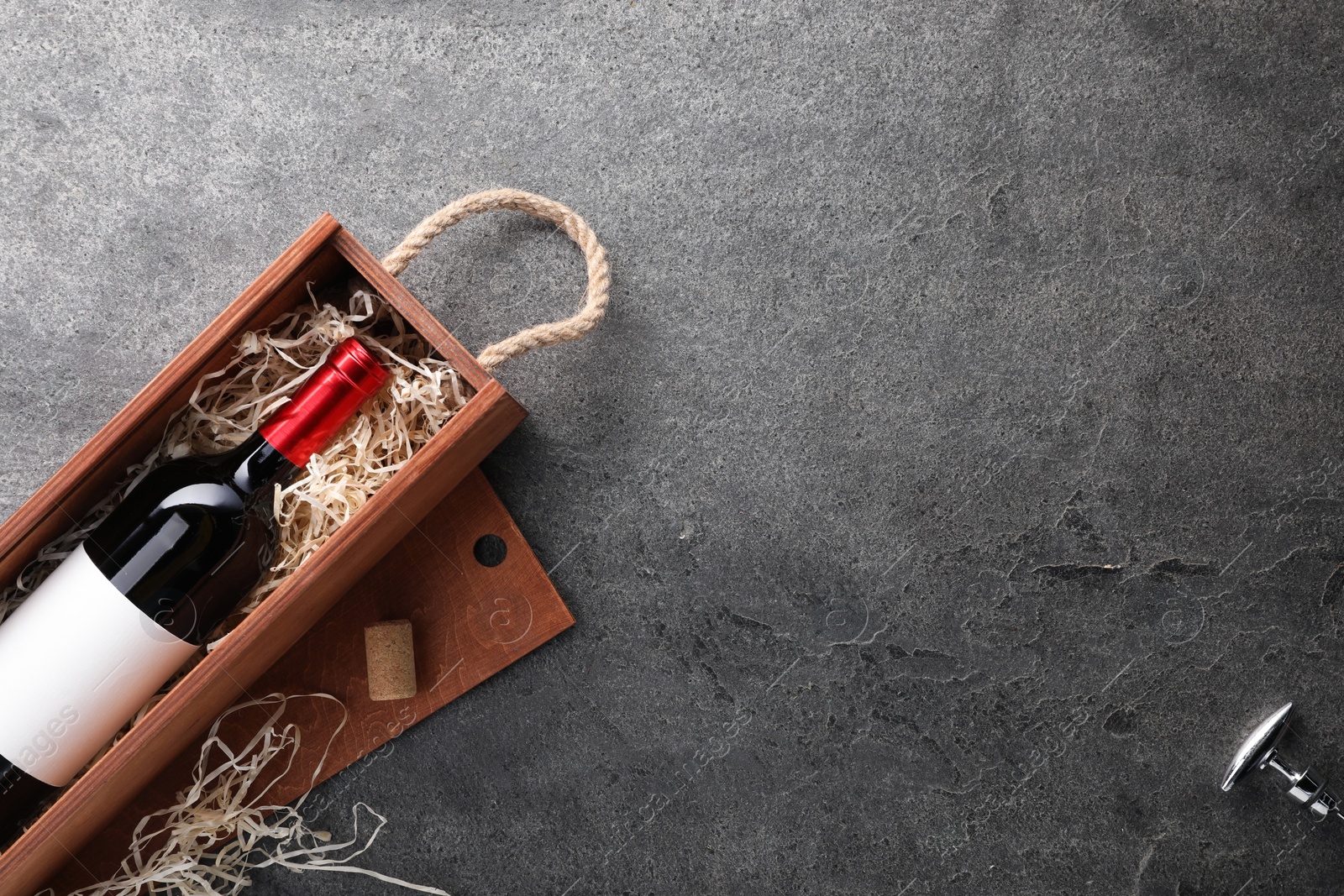 Photo of Bottle of wine in wooden box and corkscrew on dark textured table, flat lay. Space for text