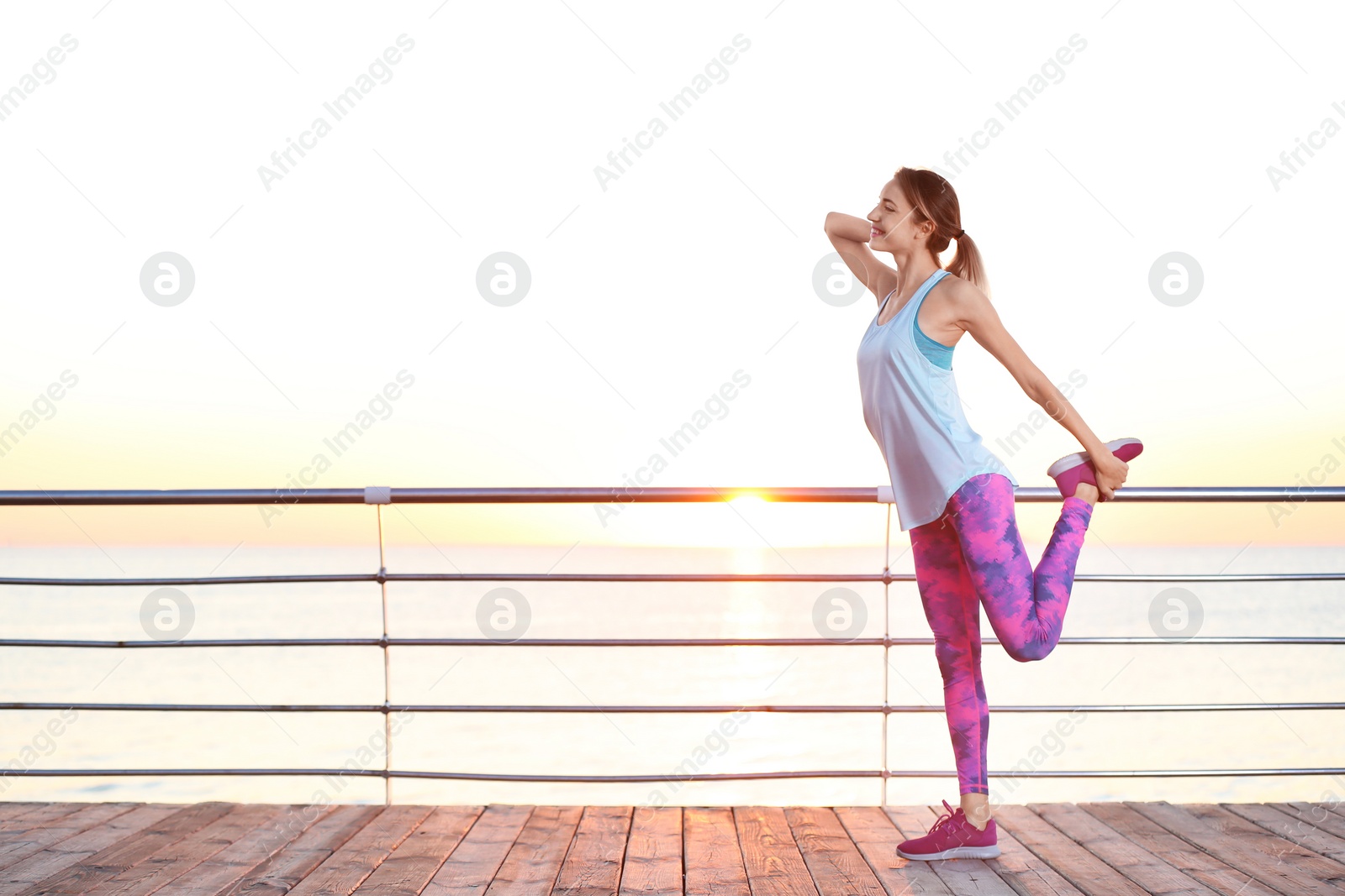 Photo of Young woman doing fitness exercises on pier in morning