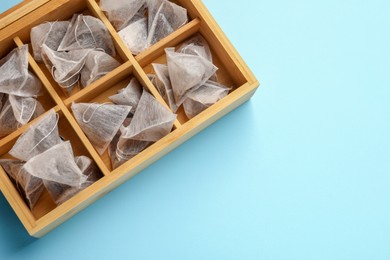 Many tea bags in wooden box on light blue background, flat lay. Space for text