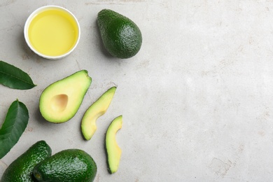 Photo of Bowl of natural oil and avocados on grey stone background, flat lay. Space for text