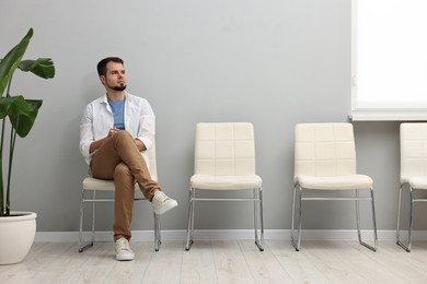 Photo of Man sitting on chair and waiting for appointment indoors