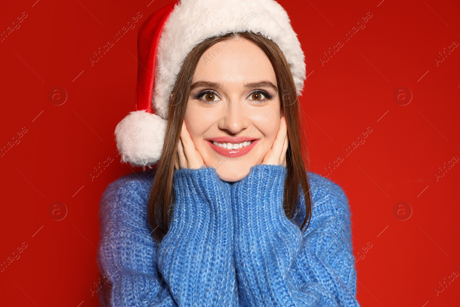 Photo of Young woman in Christmas sweater and Santa hat on red background