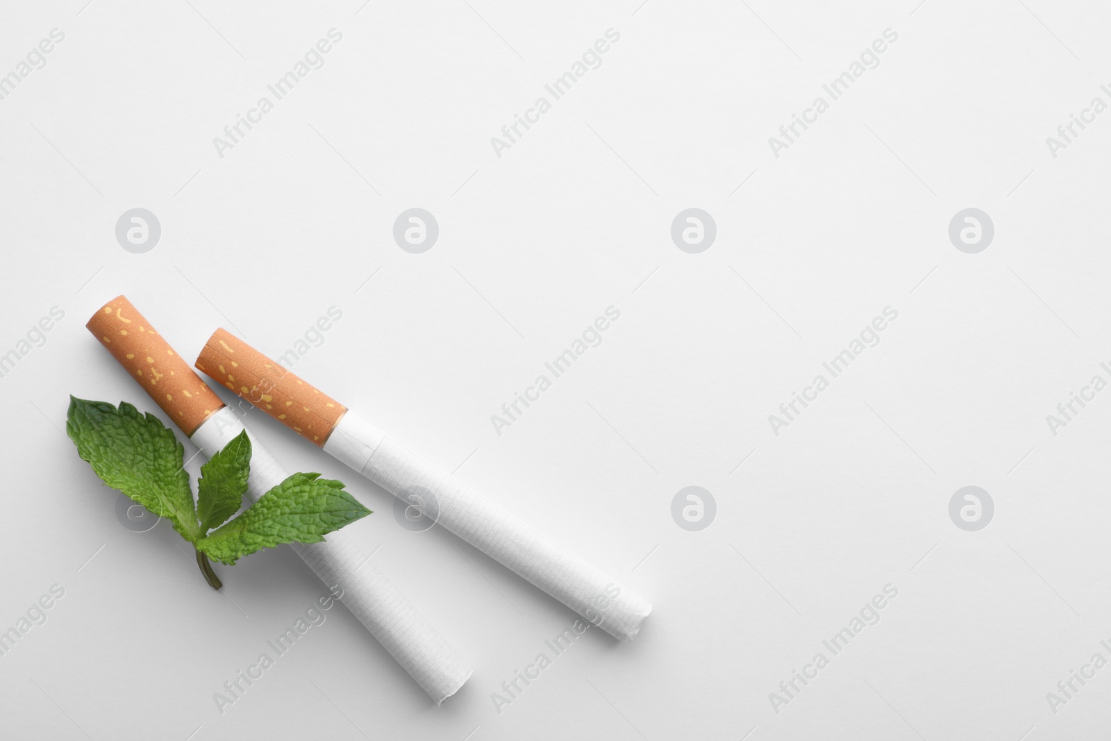 Photo of Menthol cigarettes and fresh mint leaves on white background, flat lay. Space for text