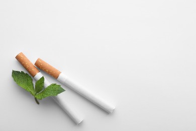 Photo of Menthol cigarettes and fresh mint leaves on white background, flat lay. Space for text