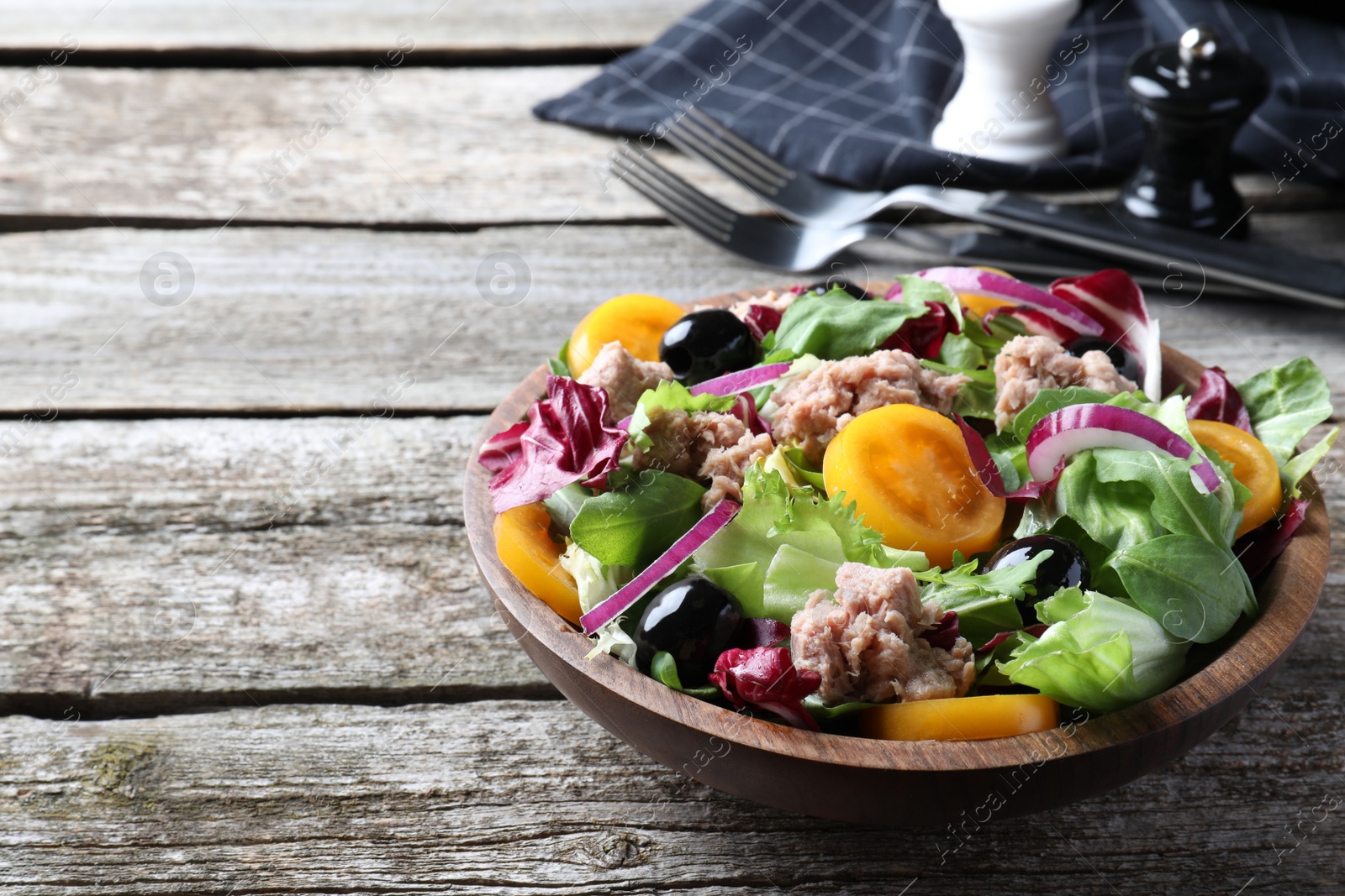 Photo of Bowl of delicious salad with canned tuna and vegetables on wooden table, space for text