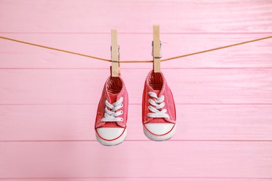 Photo of Cute baby sneakers drying on washing line against pink wooden wall