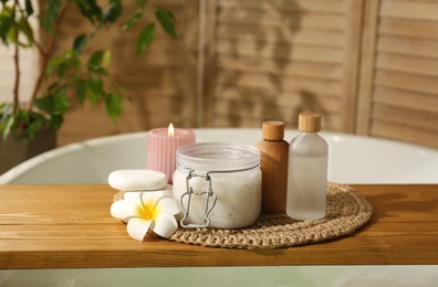 Wooden tray with spa products, stones and burning candle on bath tub in bathroom