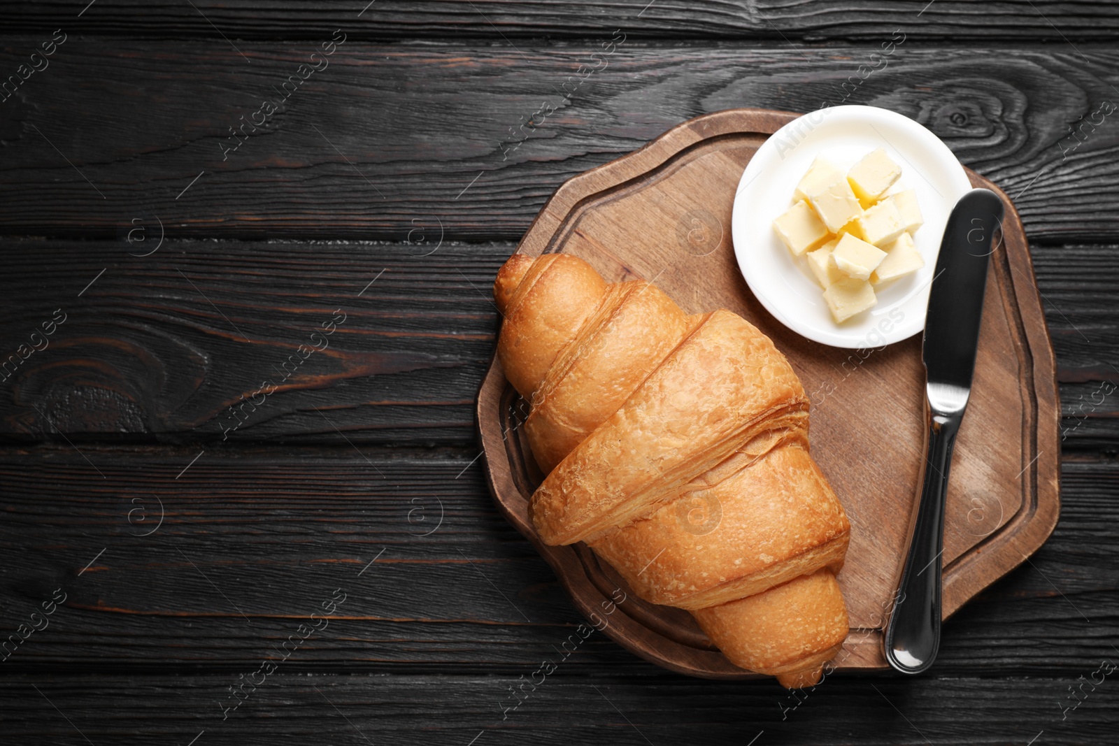 Photo of Tasty fresh croissant and butter on black wooden table, flat lay. Space for text