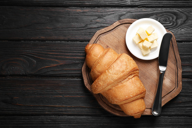 Tasty fresh croissant and butter on black wooden table, flat lay. Space for text