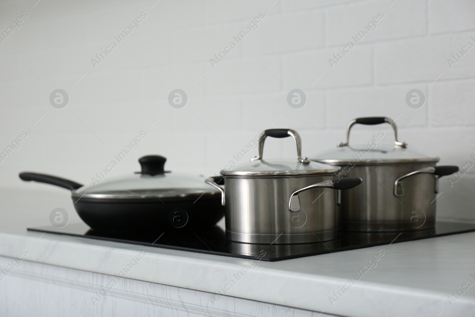 Photo of Saucepots and frying pan on induction stove in kitchen