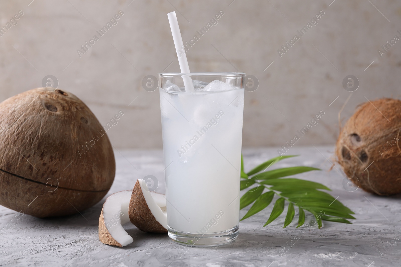 Photo of Glass of coconut water with ice cubes, palm leaf and nuts on grey table