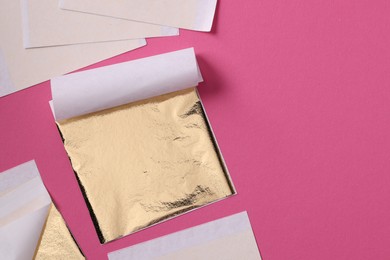 Photo of Edible gold leaf sheets on pink background, flat lay. Space for text