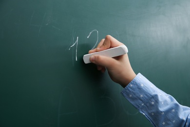 Photo of Little child writing numbers on chalkboard, closeup