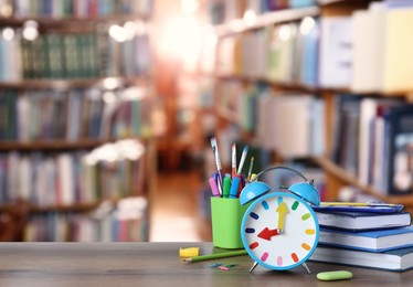 Light blue alarm clock and different stationery on wooden table in library, space for text