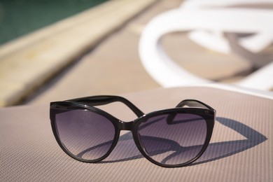 Stylish sunglasses on grey sunbed outdoors. Beach accessory, closeup